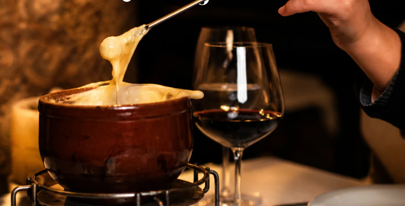 Fondue de queijo servido ao lado de uma taça de vinho
