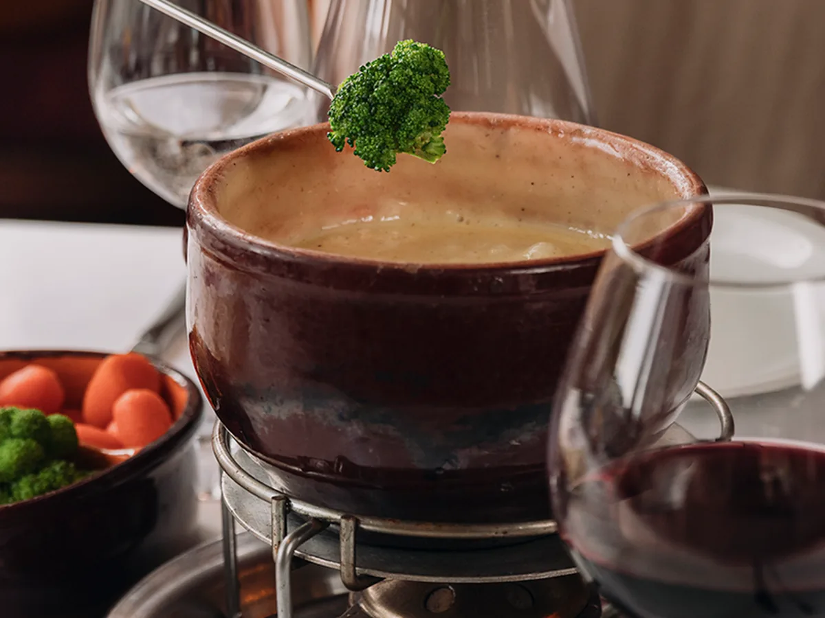 Panela de barro com fondue de queijo e um brócolis no espeto